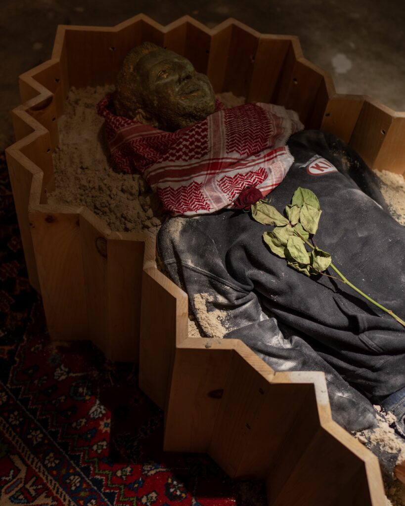 **detail** **installation** Funerary Room , 2024, Installation- Wooden Coffin, Painting on Wood, Sarcophagus in Plaster, Sand, Rug, Keffiyeh, Jeans,